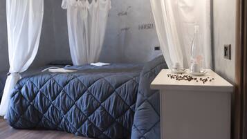 Un dormitorio con cama, cortinas blancas, una mesita de noche con una botella y vasos, y una pared con texto.