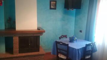 A dining area with a blue table and chairs, a fireplace, and a television mounted on the wall.