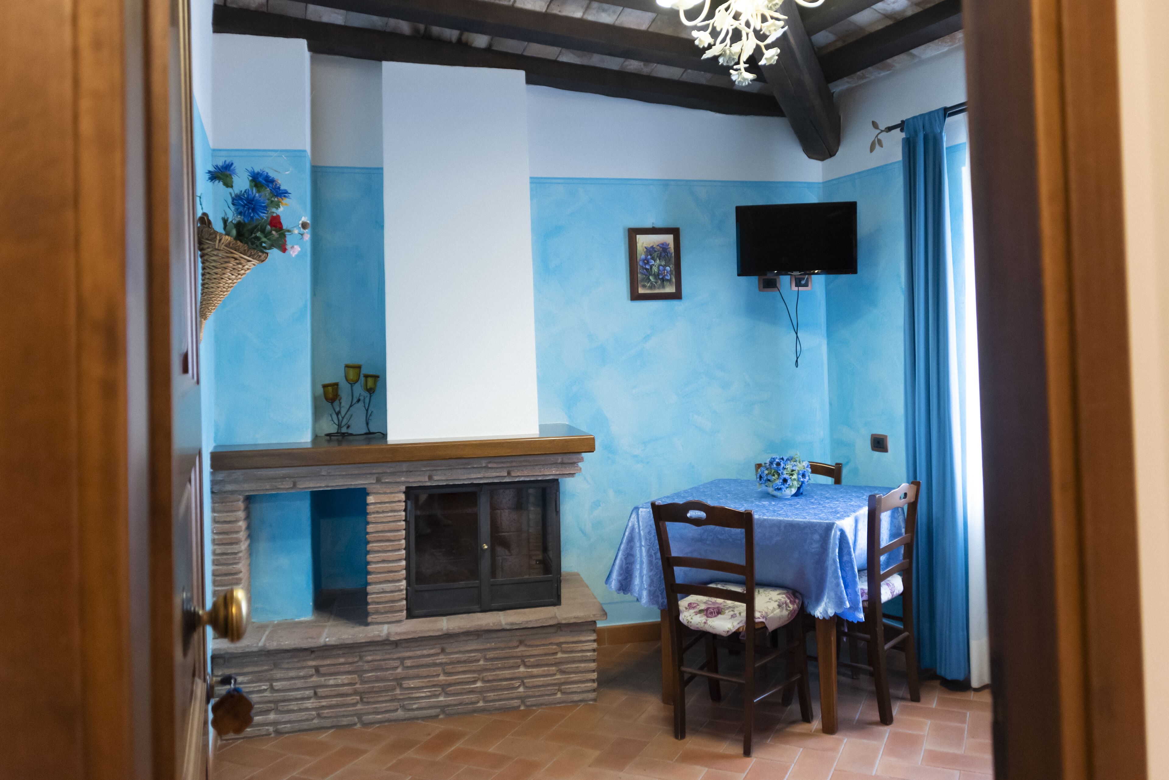 Ein Essbereich mit Kamin aus Stein, einem Tisch mit blauer Tischdecke und einem an der Wand befestigten Fernseher.