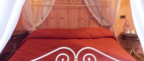 A bed with a red quilt, white curtains, and a metal headboard.