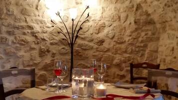 Une table dressée pour le dîner dans une pièce aux murs de pierre, agrémentée d’un chandelier servant de centre de table.