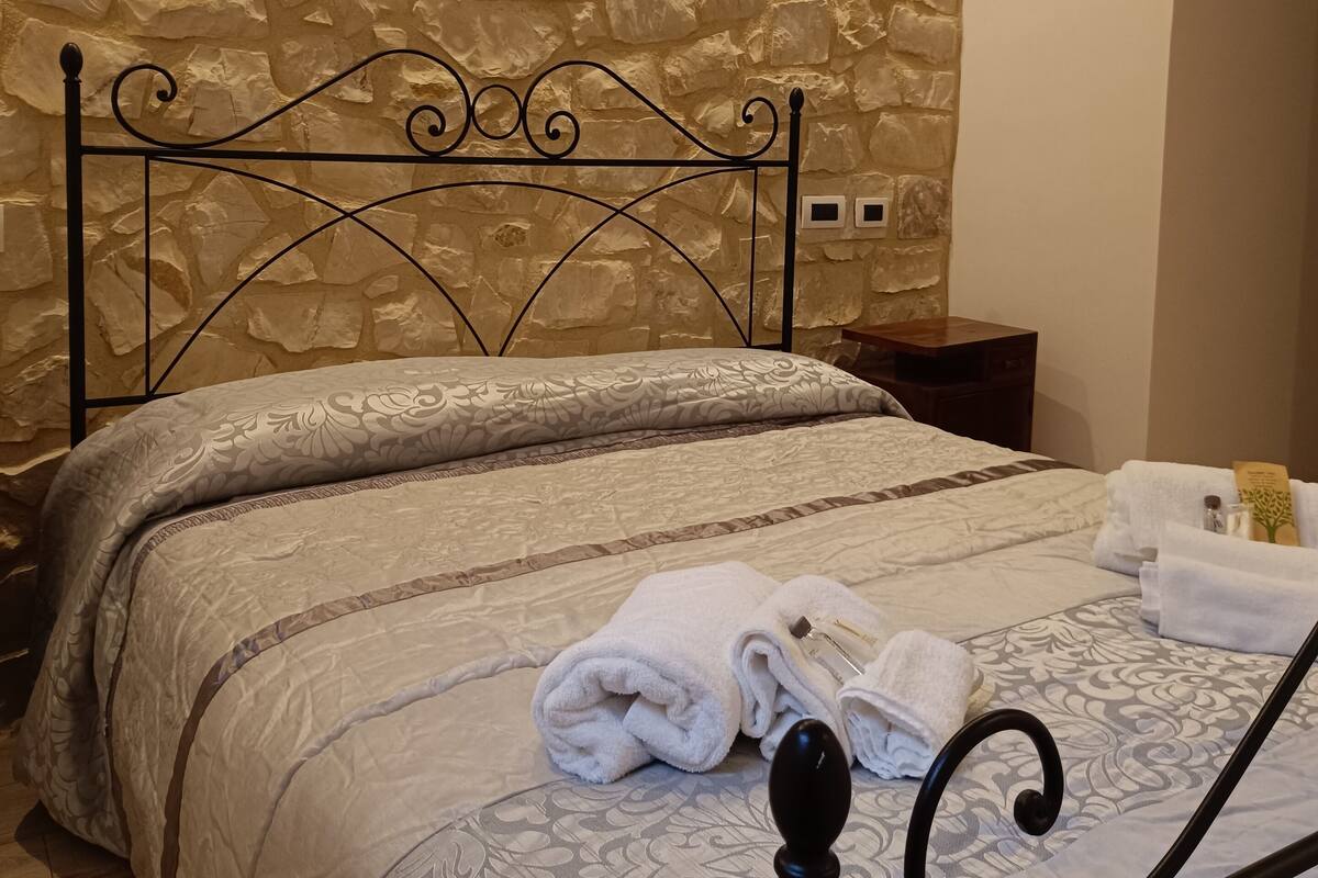 Un lit avec un mur en pierre en arrière-plan, une tête de lit en métal et des serviettes soigneusement pliées posées sur le lit.
