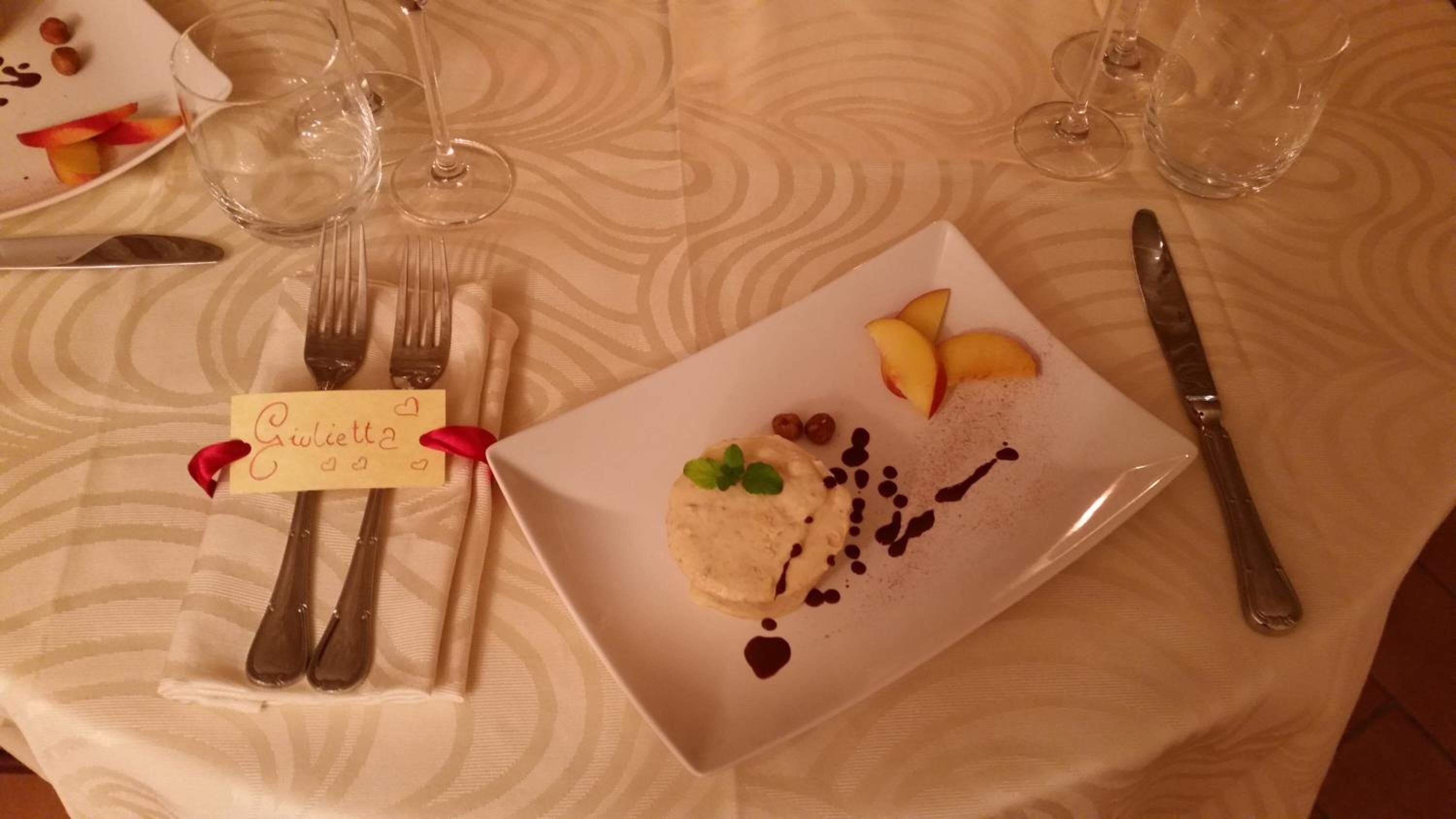 Une table dressée avec des couverts, une assiette contenant un dessert et des verres à vin.