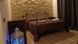 Une chambre avec un mur en pierre, un lit, une table de chevet et une lanterne décorative.