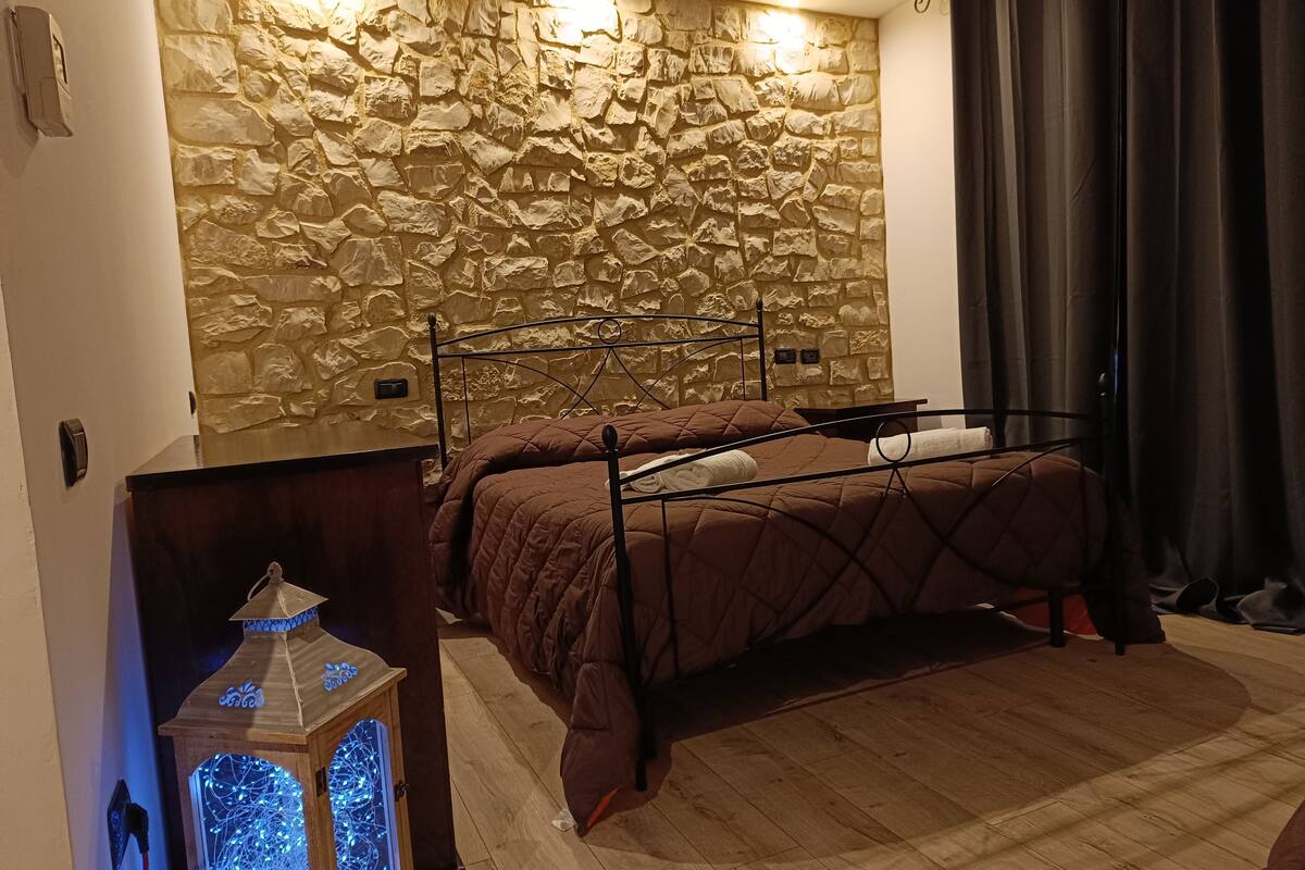 Une chambre avec un mur en pierre, un lit, une table de chevet et une lanterne décorative.