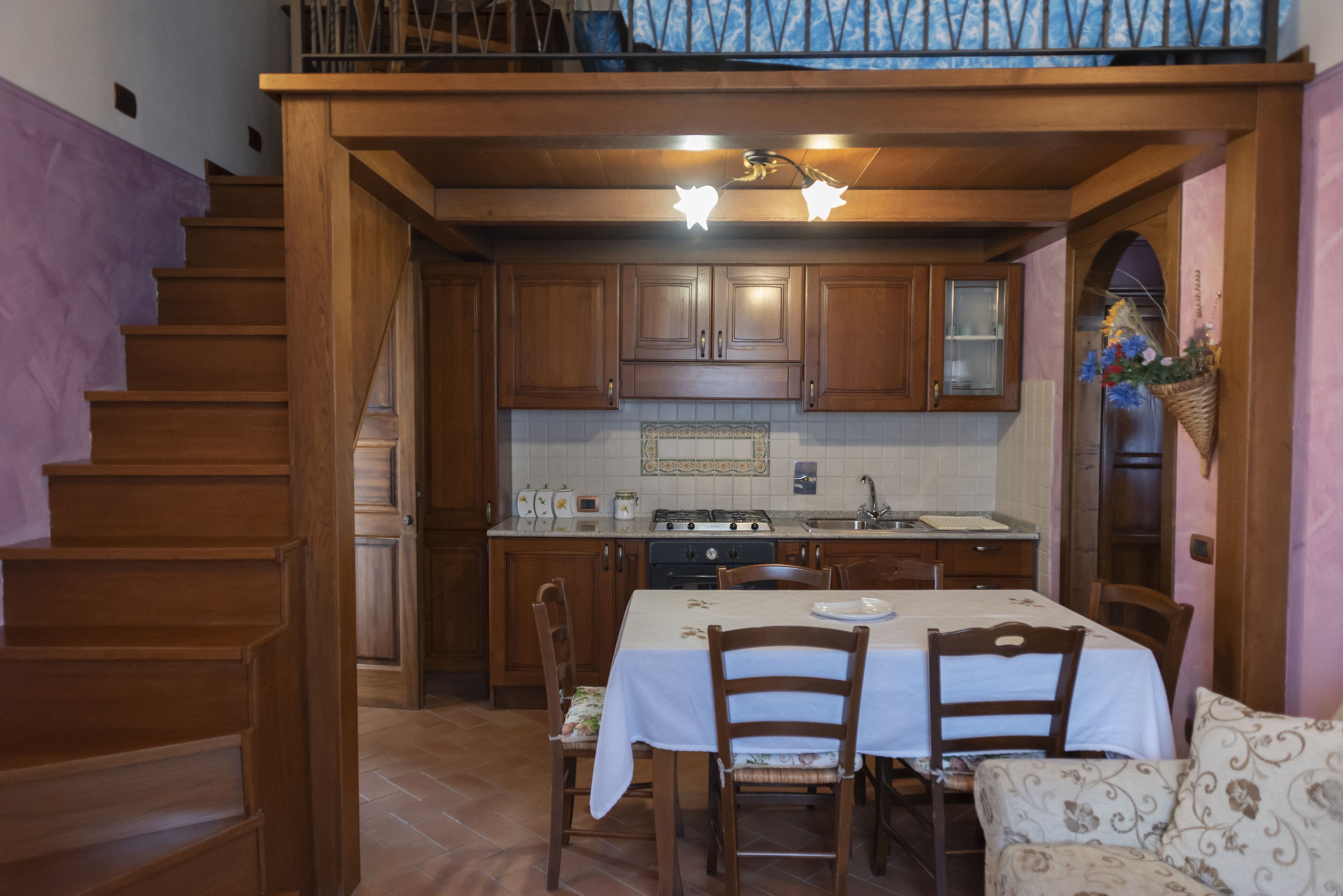 Une cuisine avec des meubles de rangement en bois, une table à manger, des chaises et un escalier.