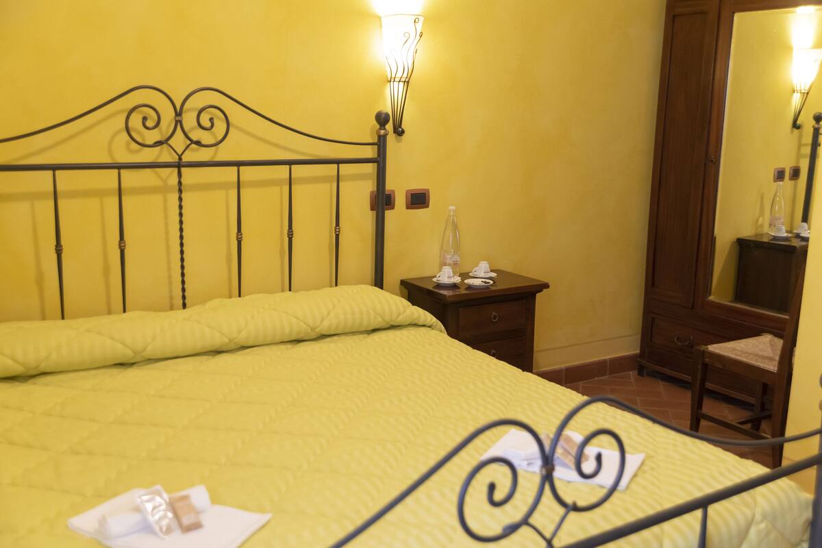 Une chambre à coucher aux couleurs jaune, avec un lit, une table de chevet et un miroir.