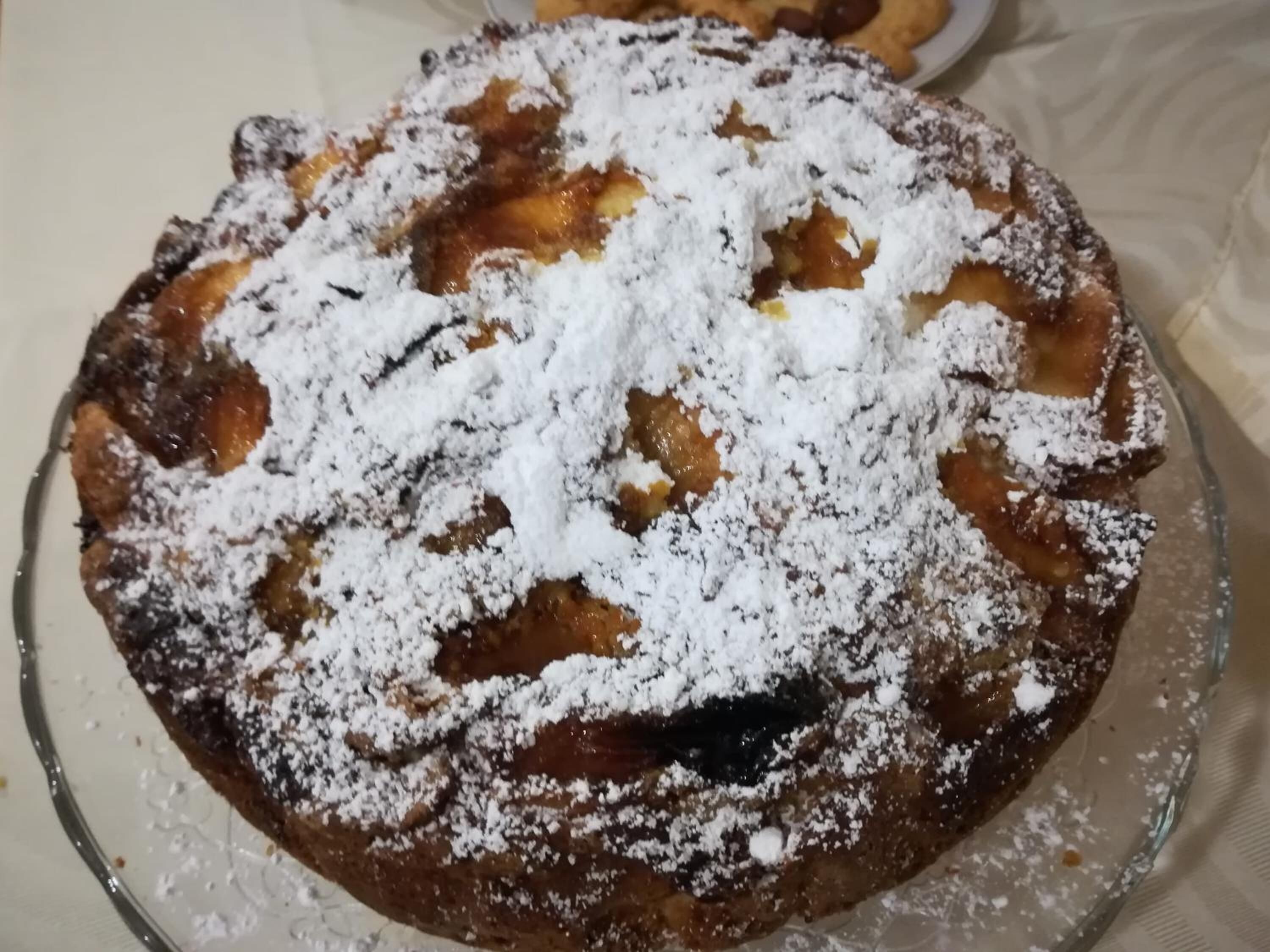 A round dessert with powdered sugar on top, served on a clear glass plate.