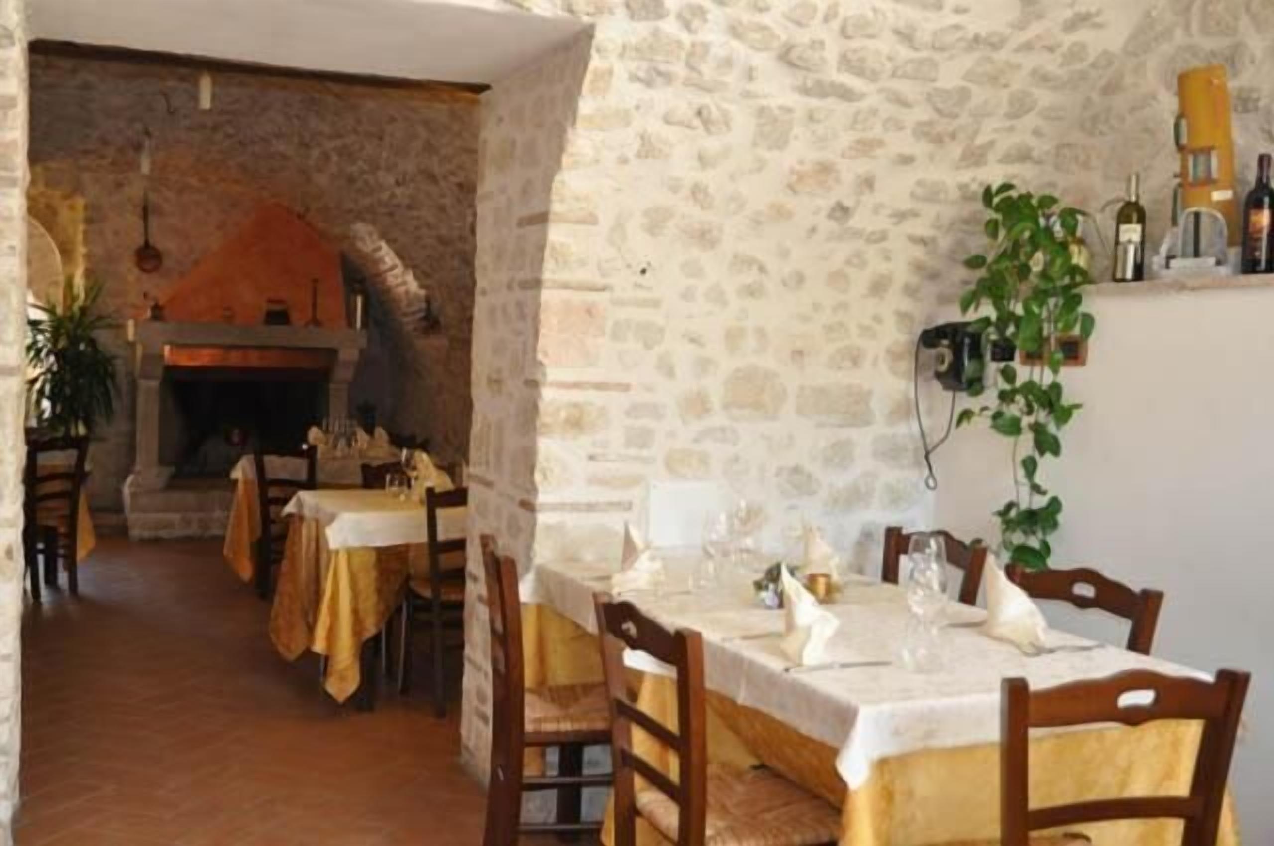 Un comedor rústico con paredes de piedra, una chimenea y una mesa para dos personas dispuesta con copas de vino y platos.