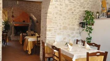 Un comedor rústico con paredes de piedra, una chimenea y una mesa para dos personas dispuesta con copas de vino y platos.