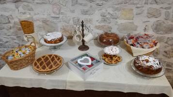 Een tafel met diverse desserts en snacks, waaronder taarten, koekjes en een gebak, voor een achtergrond van een stenen muur.