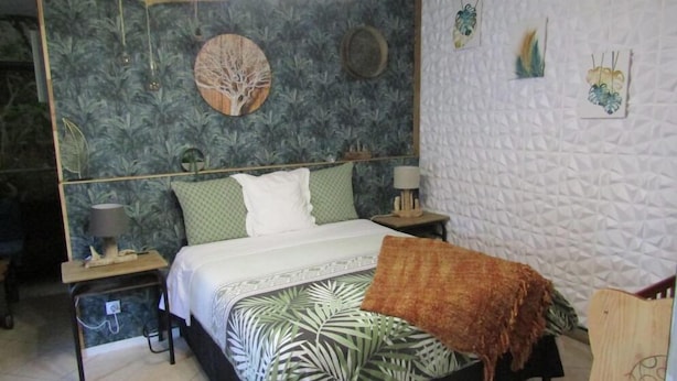 Una camera da letto con un letto, due comodini, una lampada, una sveglia a parete e un'opera d'arte con un albero decorativo.