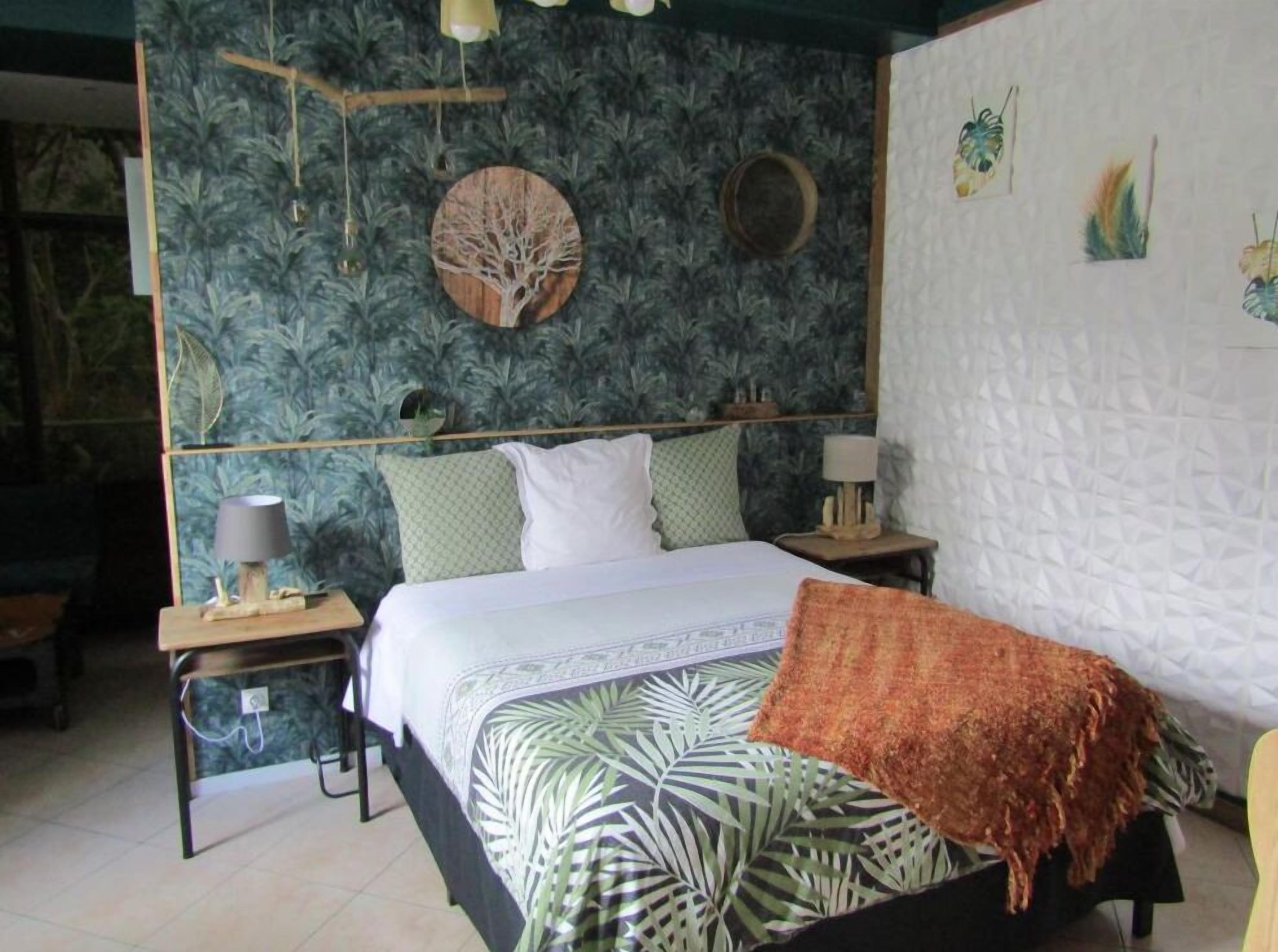 Un dormitorio con cama, dos mesitas de noche, una lámpara colgante y una pared con diseño de hojas.