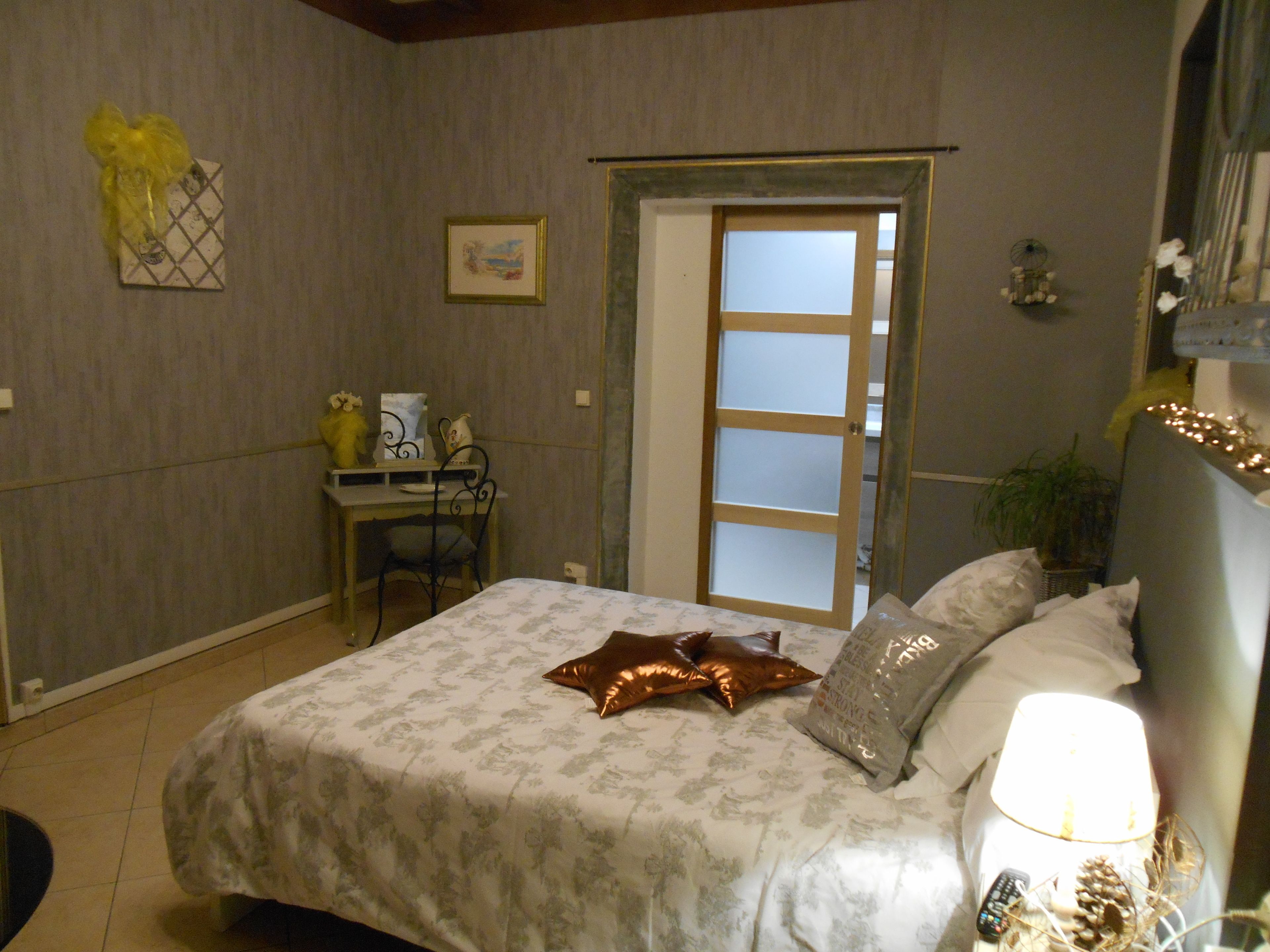A bedroom with a bed, bedside table, chair, and a door leading to another room.