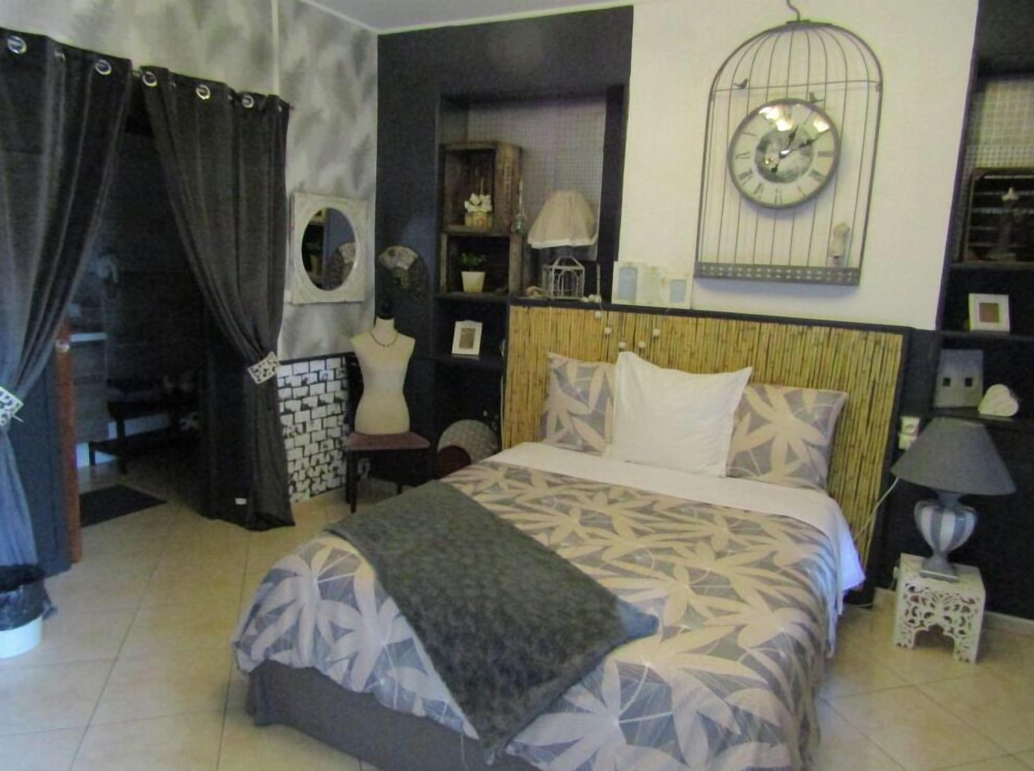 A bedroom with a bed, a nightstand, a lamp, a clock, and a wardrobe.