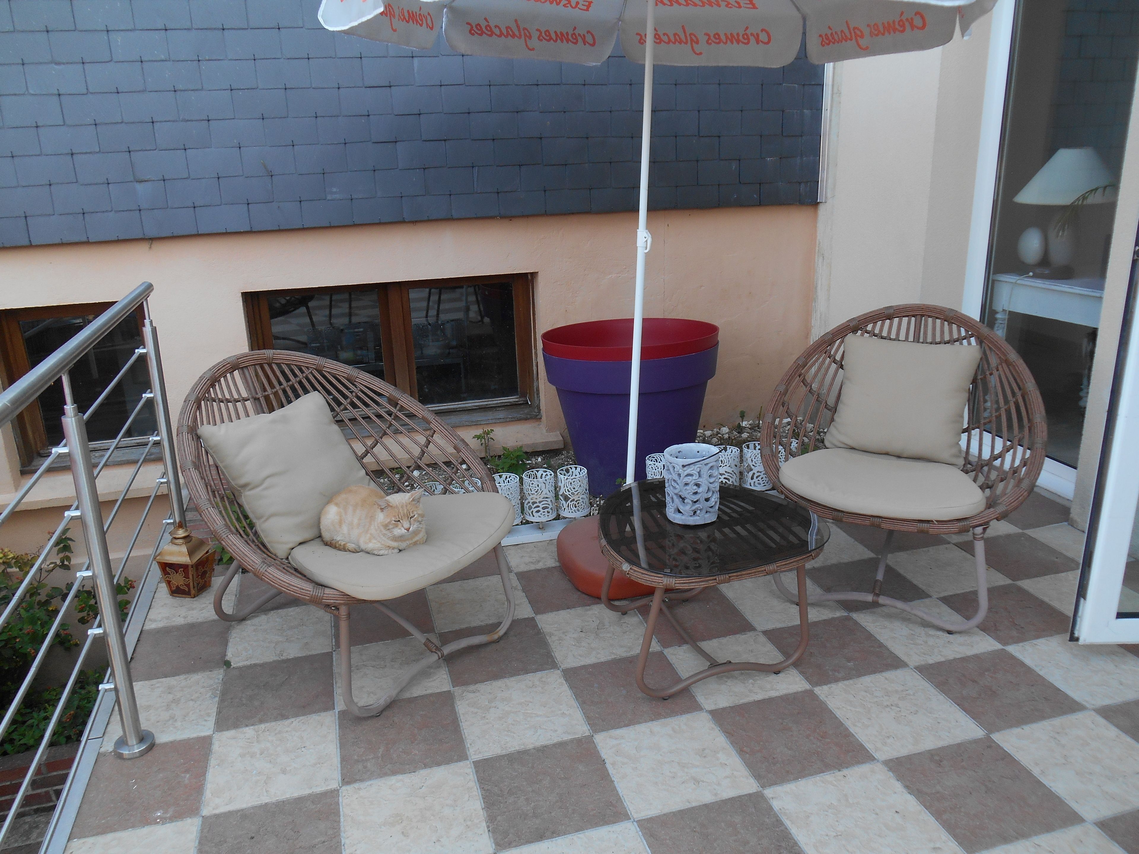 Een terras met rieten stoelen en een geruite vloer.