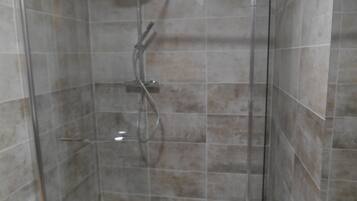 A shower with a glass door, a handheld showerhead, and a wall-mounted faucet.
