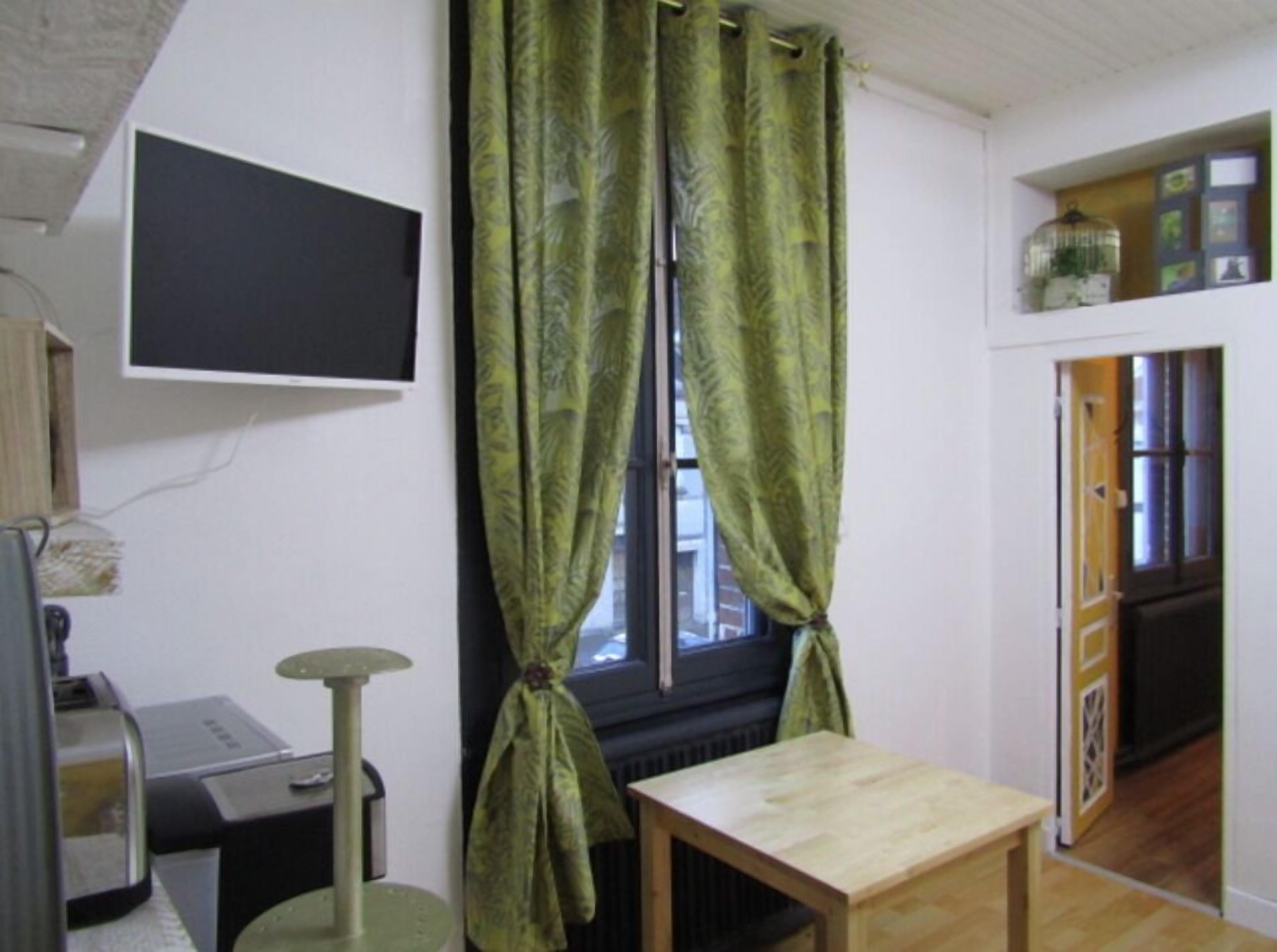 A room with a window, a flat-screen TV mounted on the wall, a small wooden table, and a cat tree.