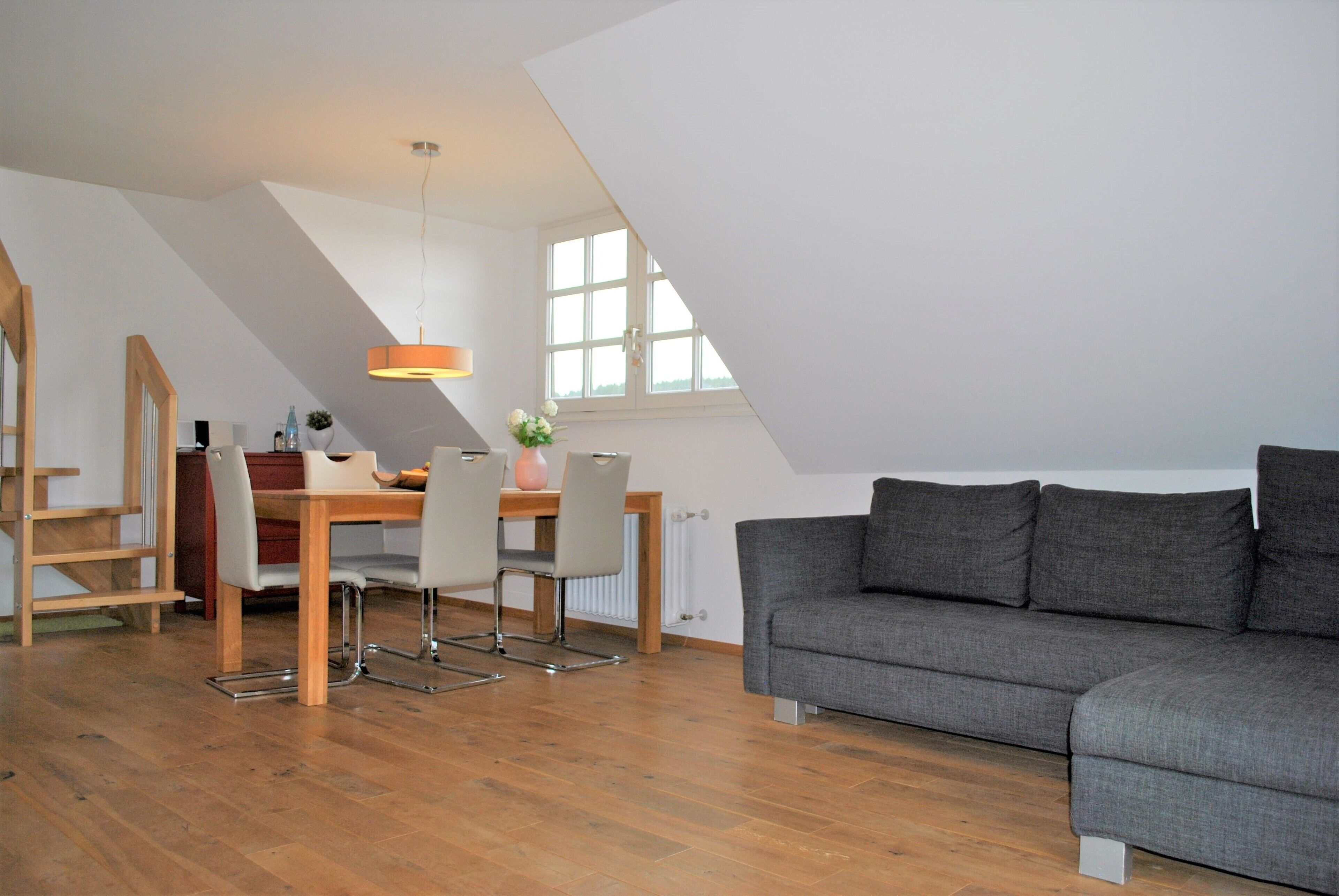 A modern loft apartment with a dining area, gray sofa, and wooden flooring.