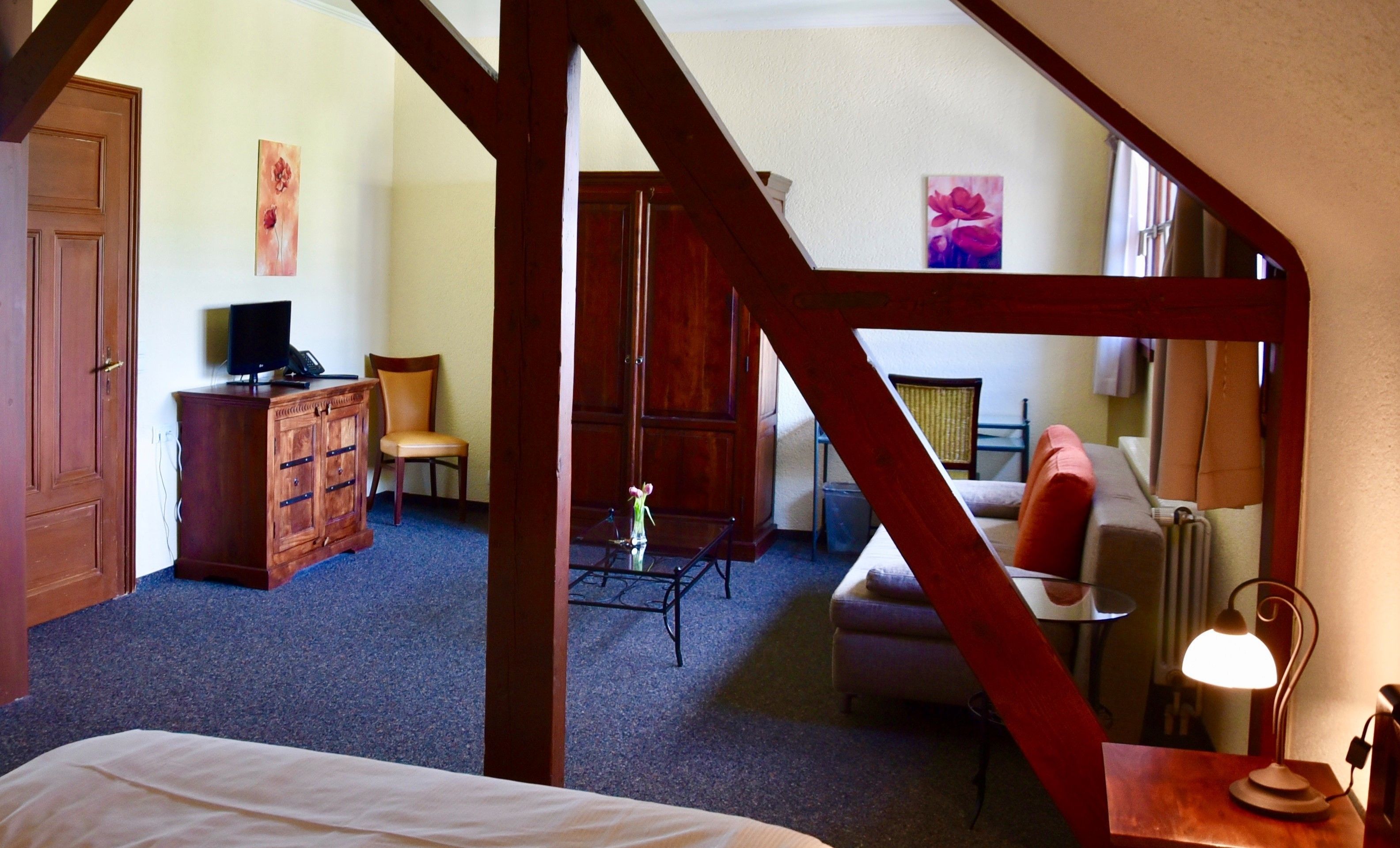 A bedroom with a bed, a desk, a chair, a dresser, and a lamp.