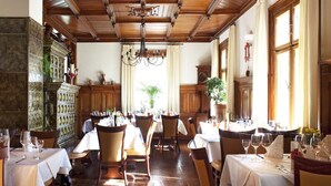 A dining area with wooden tables and chairs, a chandelier, and a large cabinet with decorative items. - Hotel & Chalets Herrihof (Todtnau)