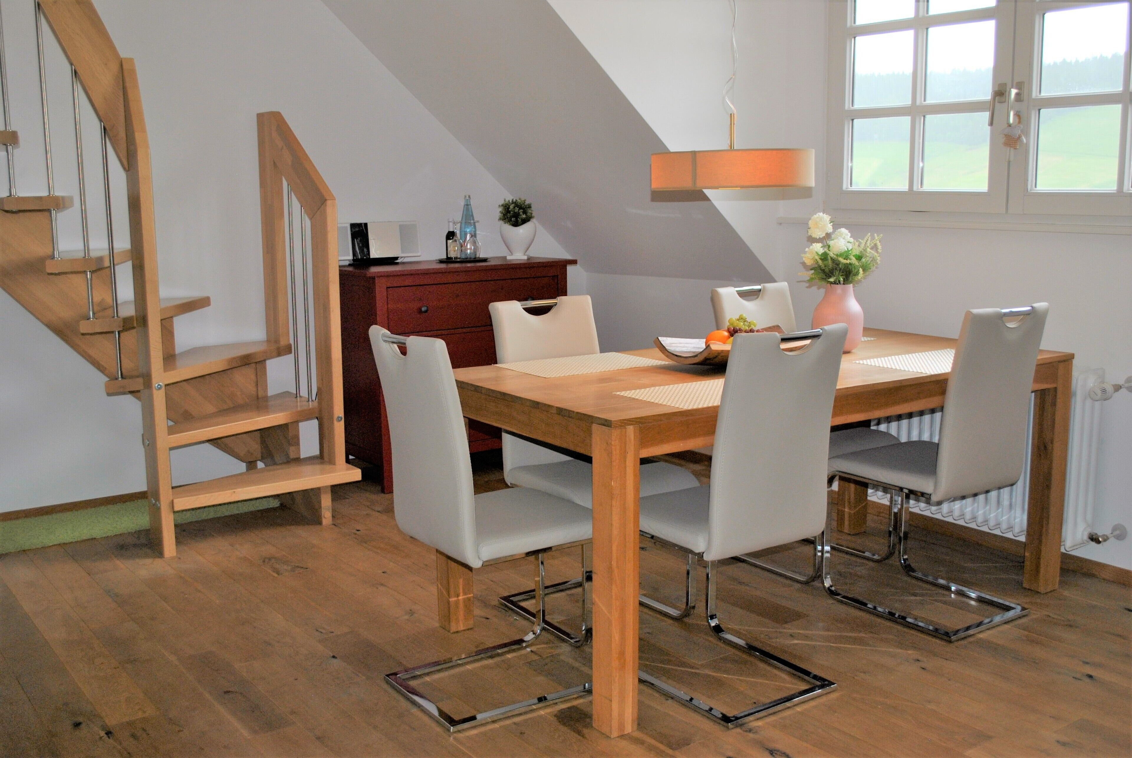 A dining area with a wooden table, white chairs, and a vase of flowers.
