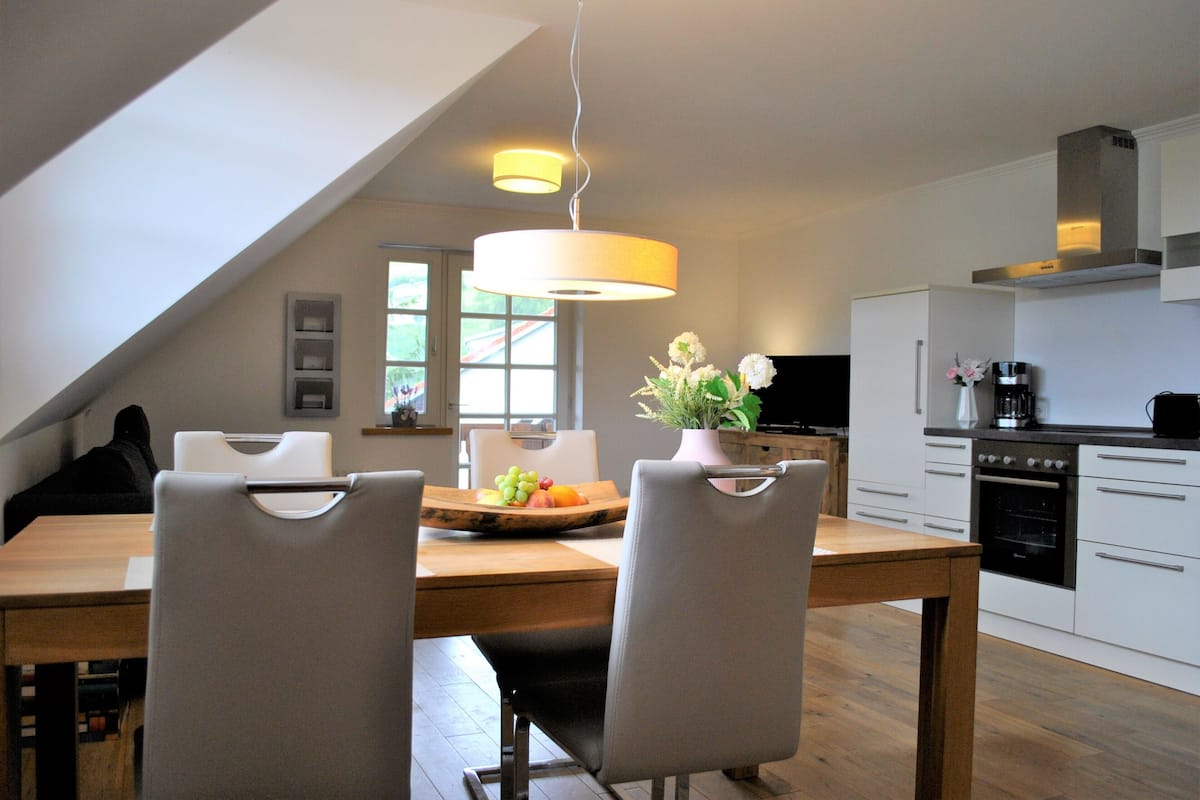 A modern kitchen with white cabinets, a wooden dining table, and two chairs.