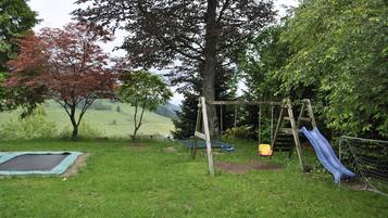 A grassy outdoor area with a swing set, a slide, and a trampoline.