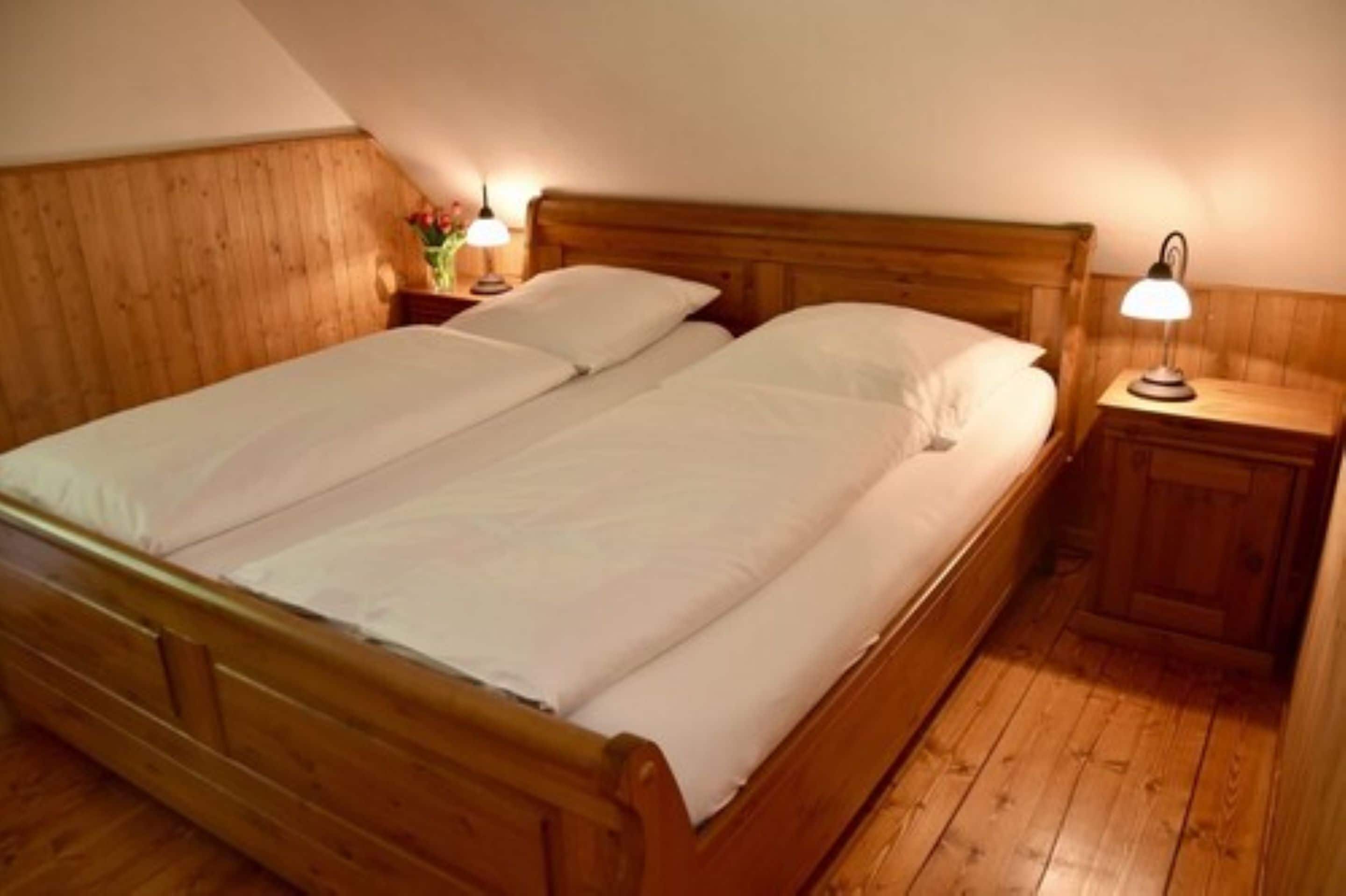 A double bed with wooden headboard and footboard, two bedside tables with lamps, and a wooden floor.