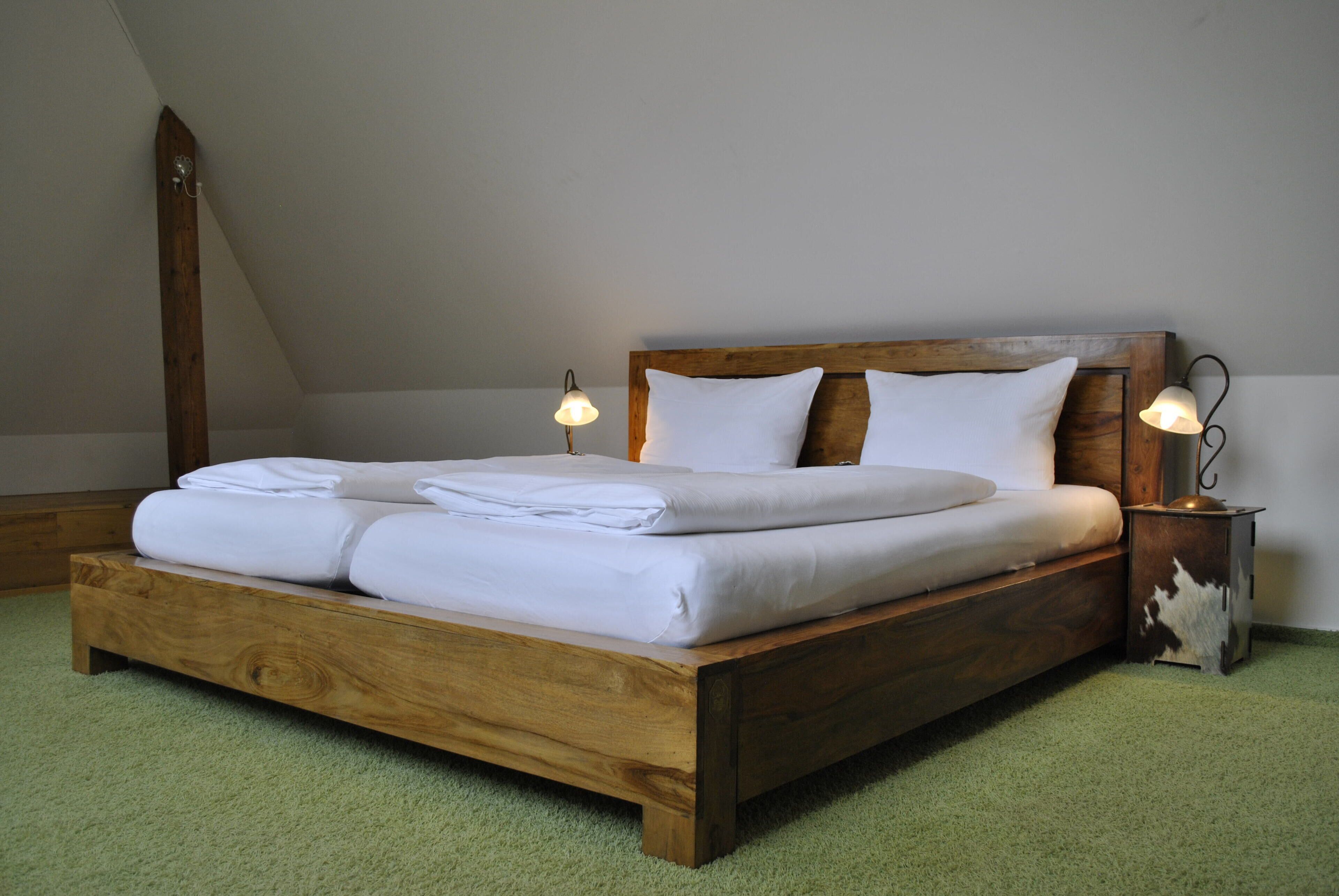 Ein hölzernes Bett mit weißer Bettwäsche in einem Zimmer mit geneigter Decke und grünem Teppich.