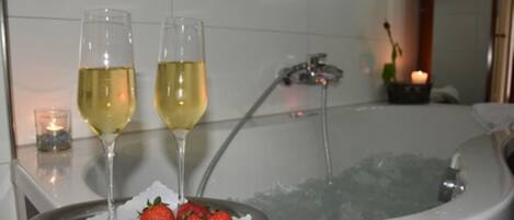A bathtub with two glasses of white wine and a plate of strawberries.