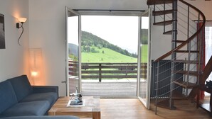A living room with a sofa, a coffee table, a lamp, and a view of a green landscape through a glass door. - Hotel & Chalets Herrihof (Todtnau)