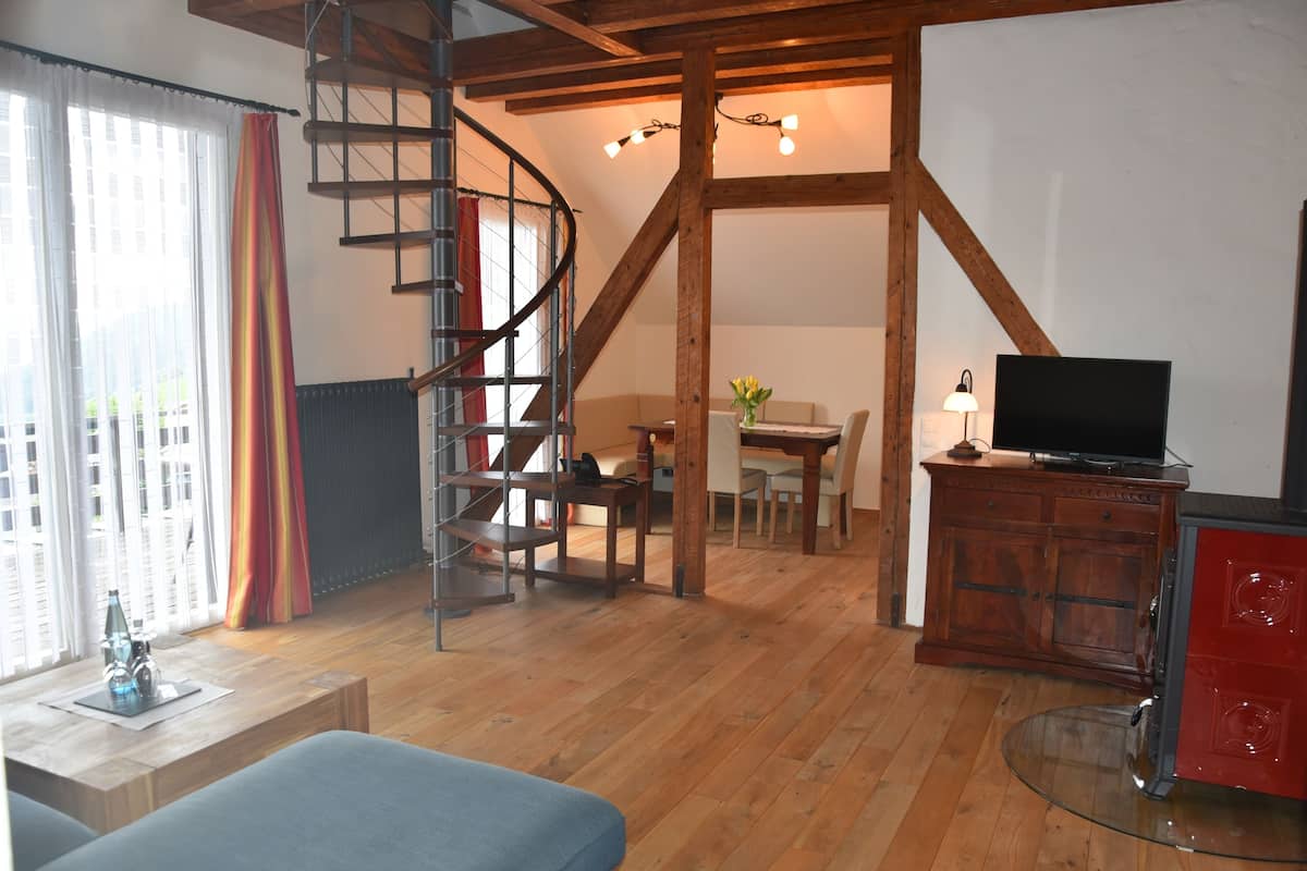 A spacious living area with a spiral staircase, wooden flooring, a dining table, and a television on a cabinet.
