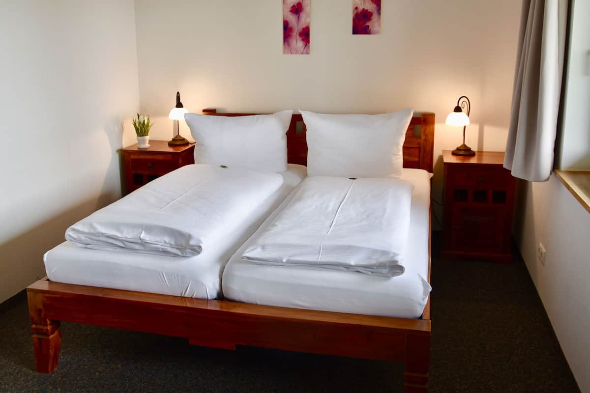 A double bed with white linens, two bedside tables with lamps, and two wall-mounted flower paintings.