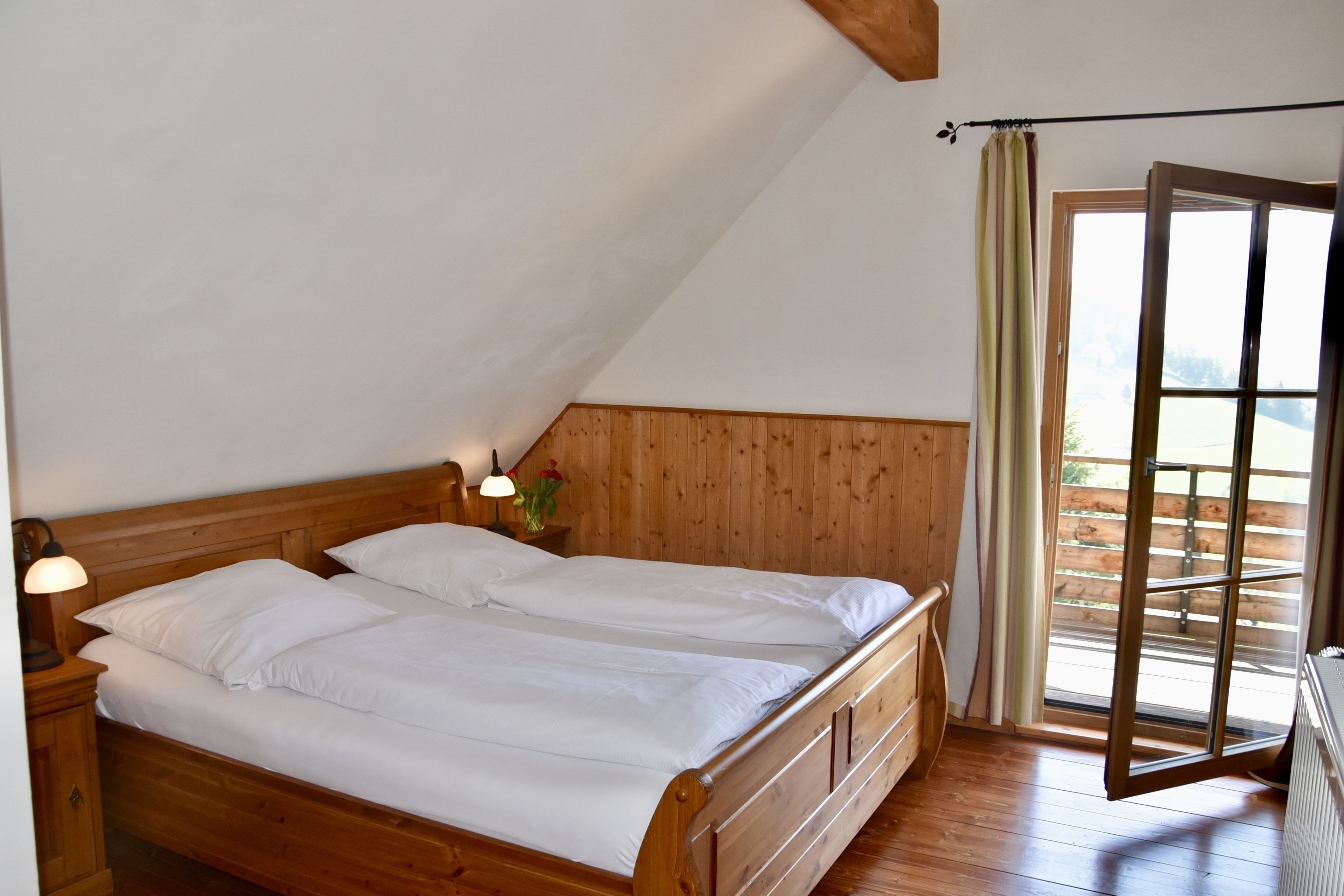 A bedroom with a wooden bed, a nightstand with a lamp, and a window with curtains.