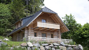 A log cabin with a balcony, surrounded by a stone wall and lush greenery. - Hotel & Chalets Herrihof (Todtnau)