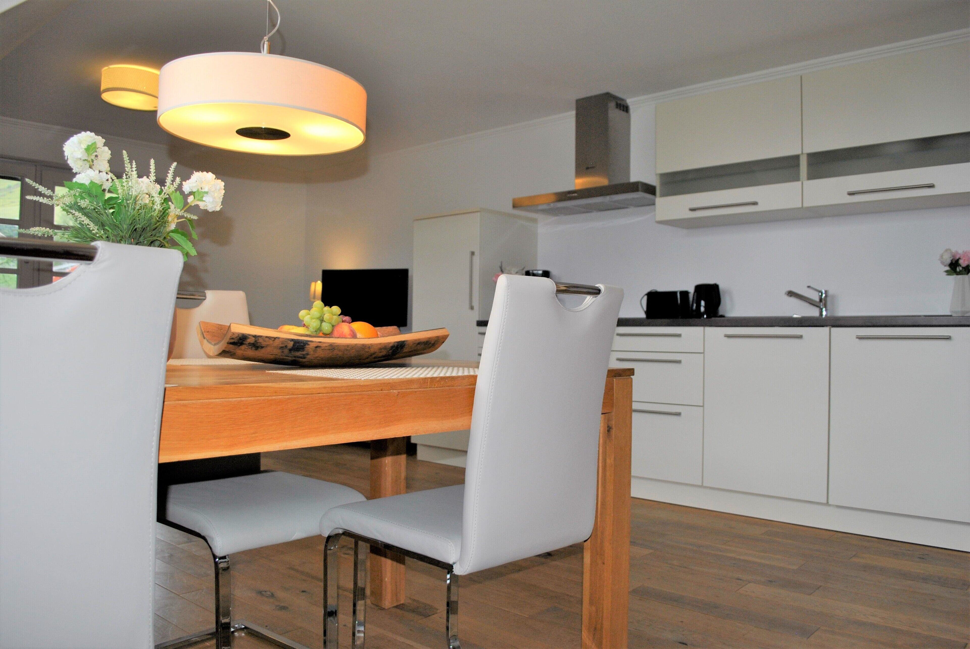 A modern kitchen with white cabinets, a wooden dining table, and two chairs.