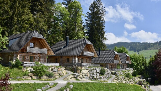 A log cabin-style hotel with multiple buildings, stone pathways, and a mountainous backdrop. - Hotel & Chalets Herrihof (Todtnau)
