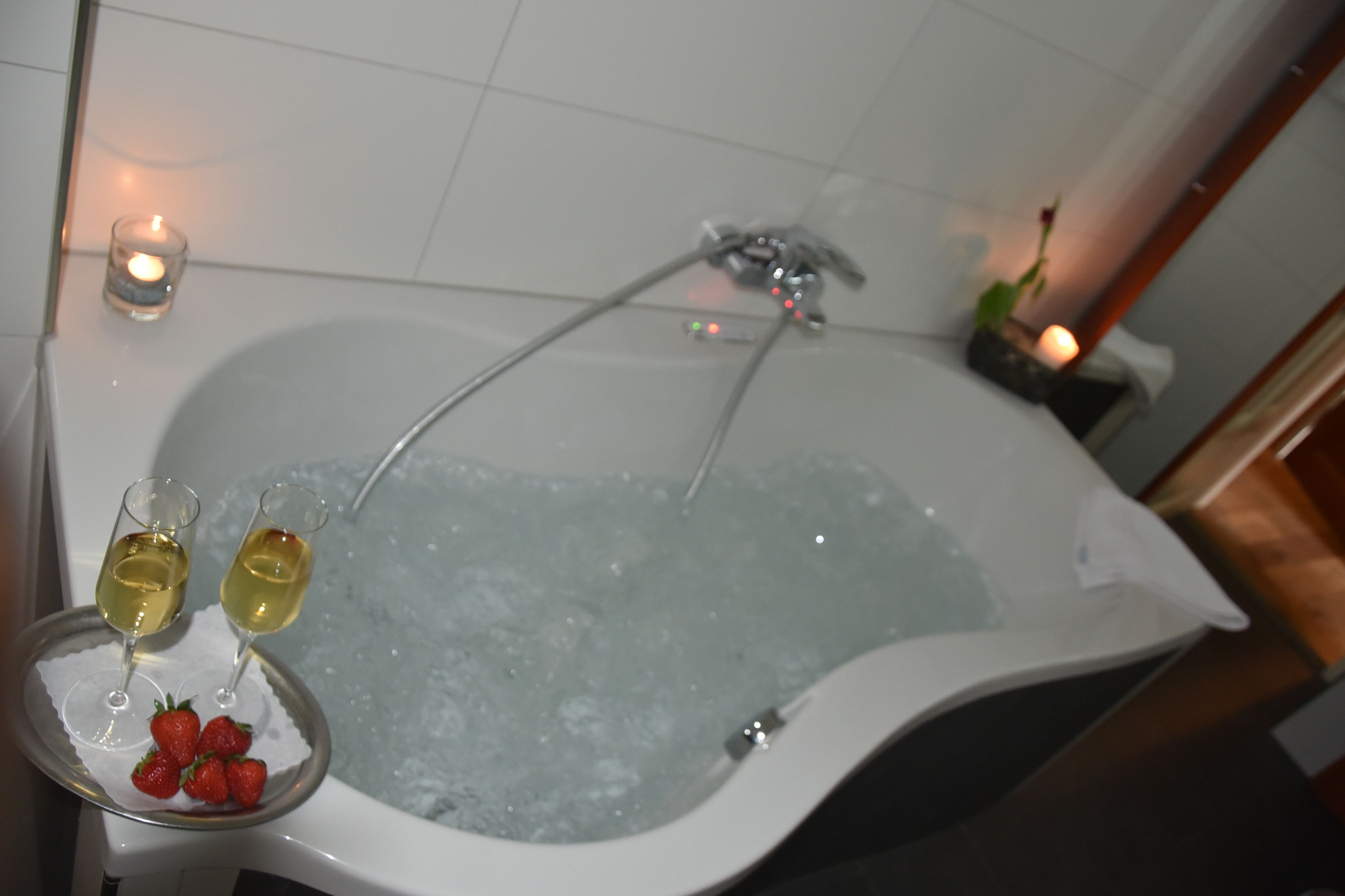 A bathtub with two glasses of white wine and strawberries on a tray.
