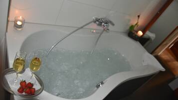 A bathtub with two glasses of white wine and strawberries on a tray.