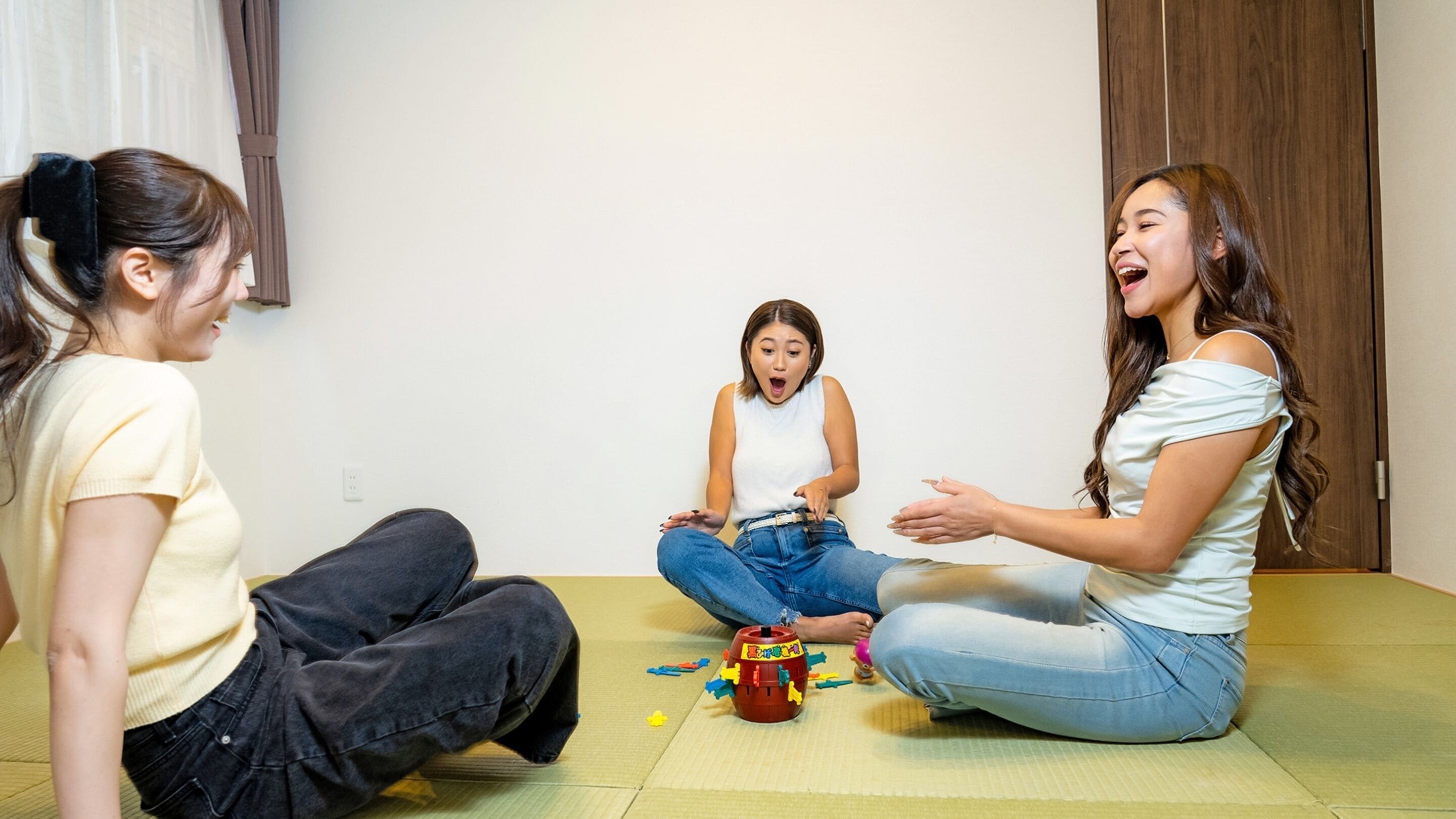 Three people sitting on a mat in a room with a wooden door and a white wall.