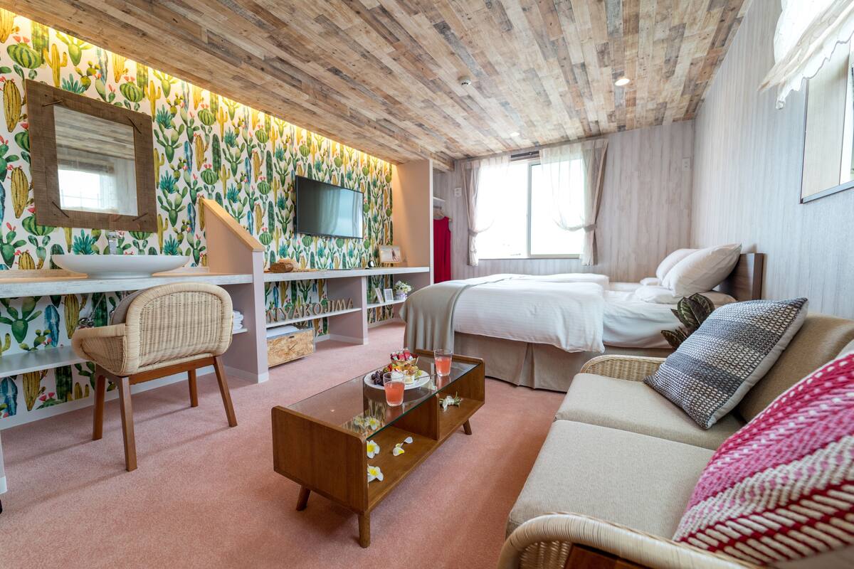 Une pièce chaleureuse avec un plafond en bois, un lit, un canapé, une télévision et un mur décoré sur le thème des cactus.