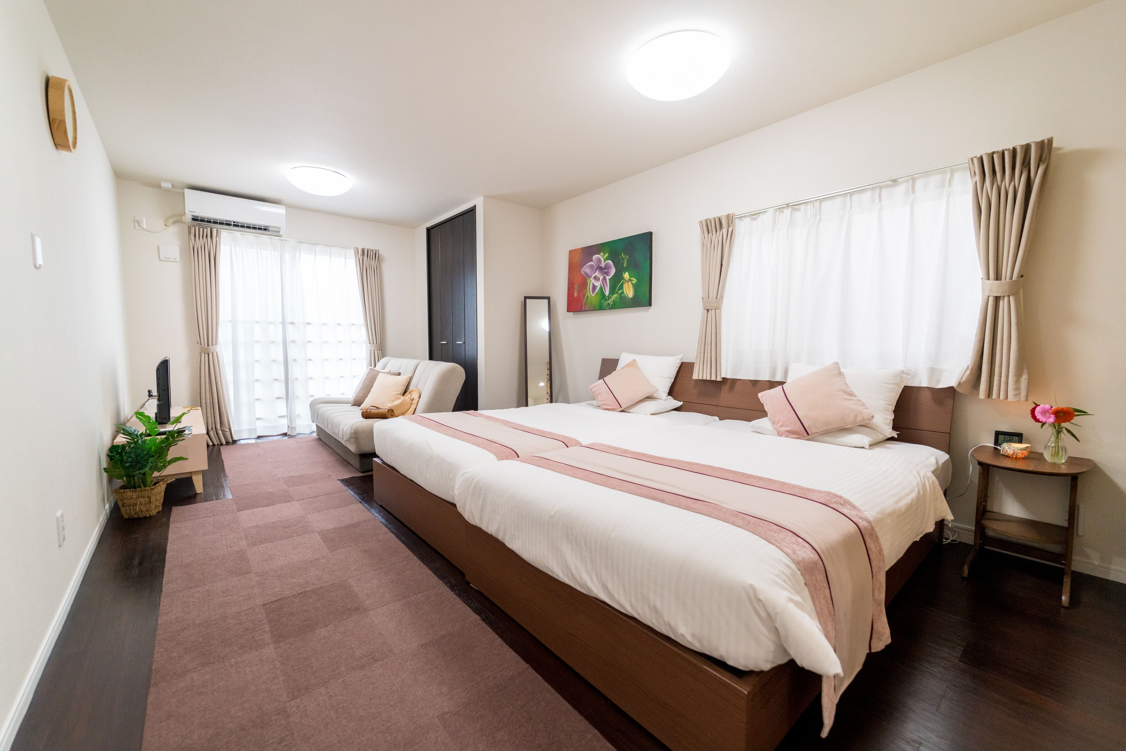 A modern bedroom with a large bed, a bedside table, a mirror, and a potted plant.