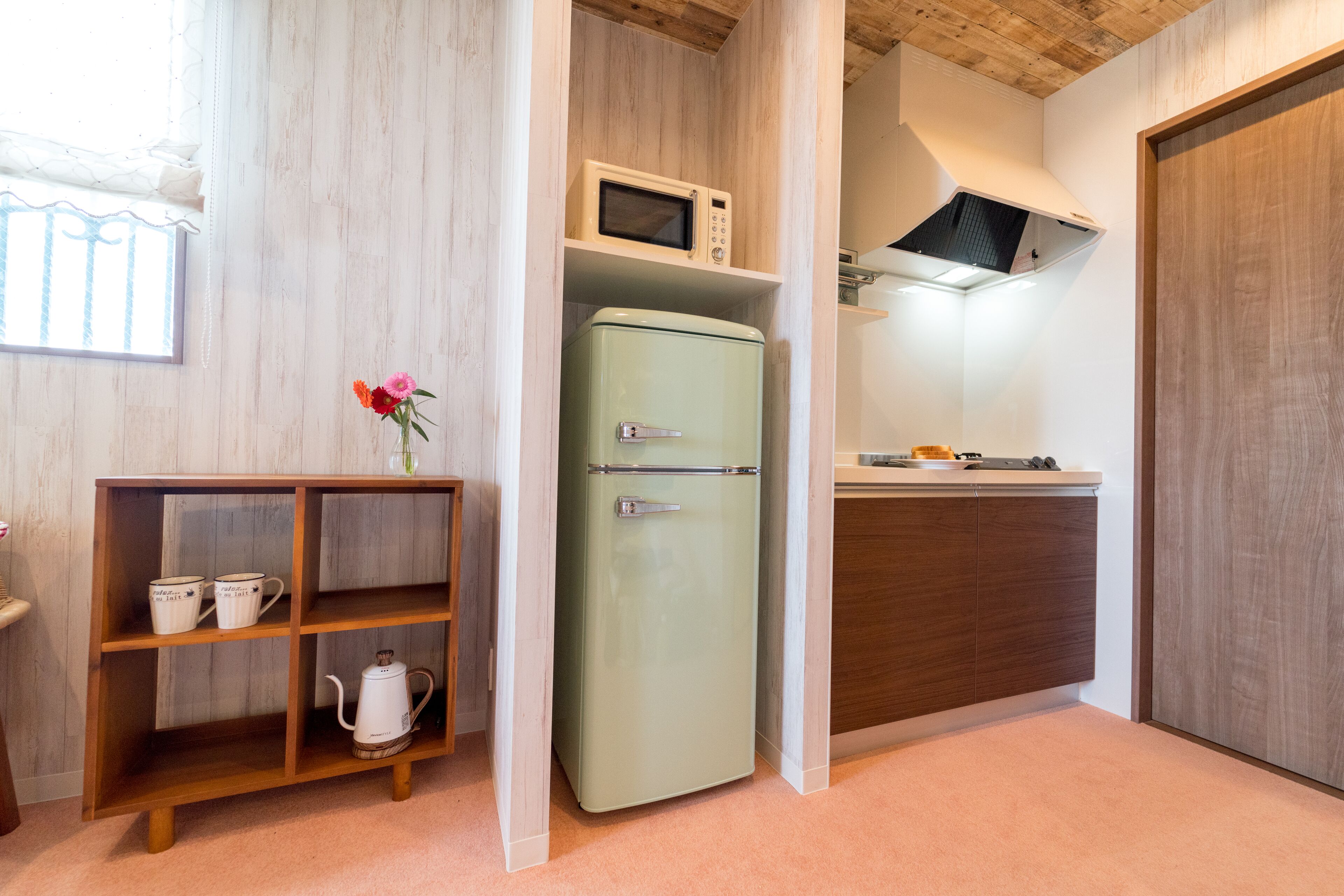 Una cocina compacta con un refrigerador de estilo vintage, un microondas y una repisa de madera con utensilios de cocina.
