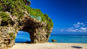Formación rocosa natural con una abertura parecida a un túnel, una playa arenosa y agua azul cristalina.