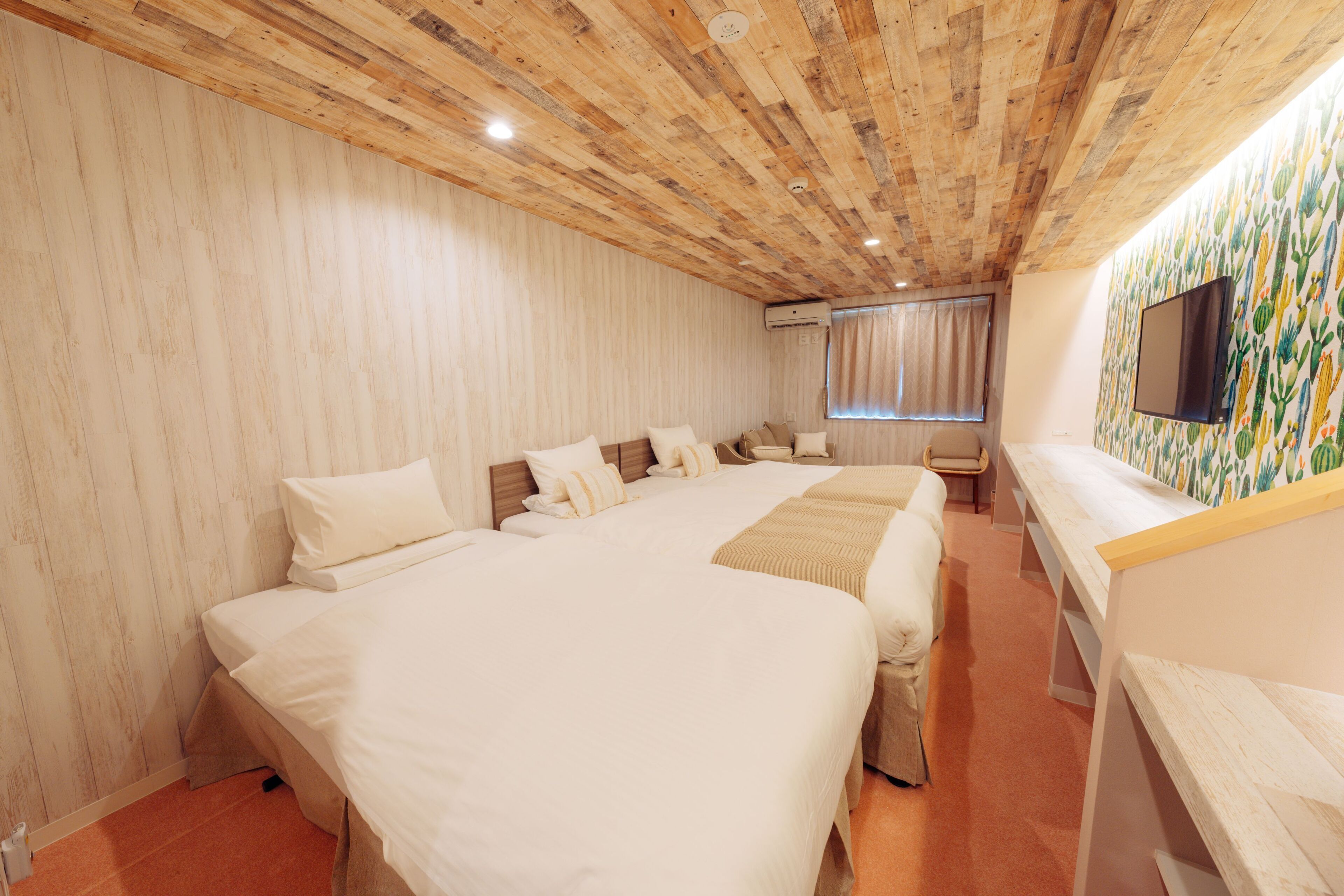 A hotel room with a wooden ceiling, a large bed, a desk, and a TV on the wall.