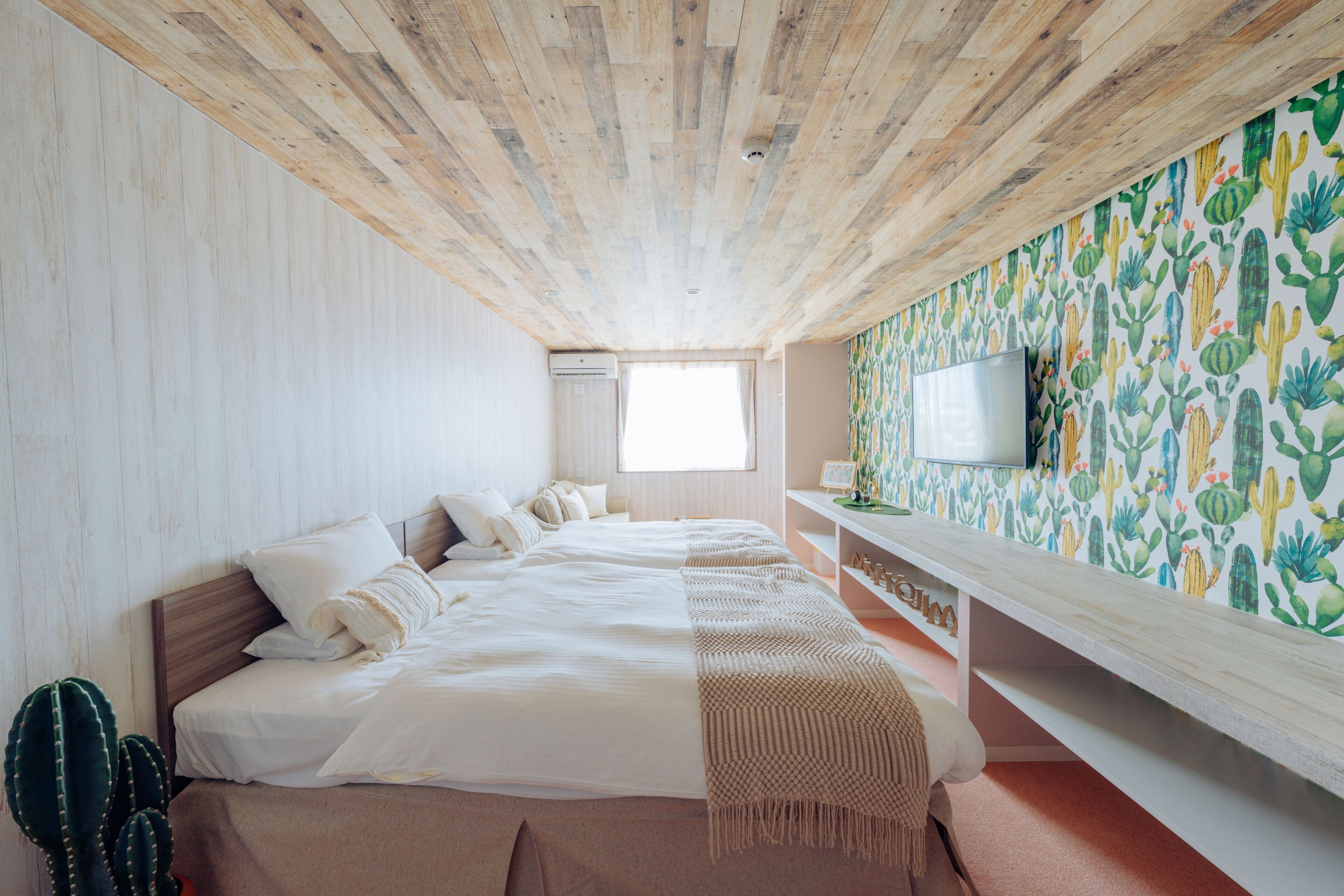 A bedroom with a wooden ceiling, a bed with white bedding, a cactus decoration, and a wall with a cactus pattern.