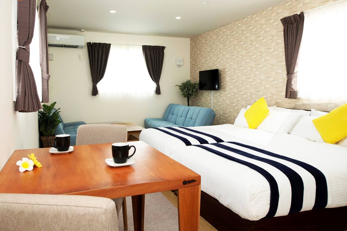 Une chambre d’hôtel avec un lit, un canapé, une table avec une tasse et une fleur, et un téléviseur fixé au mur.