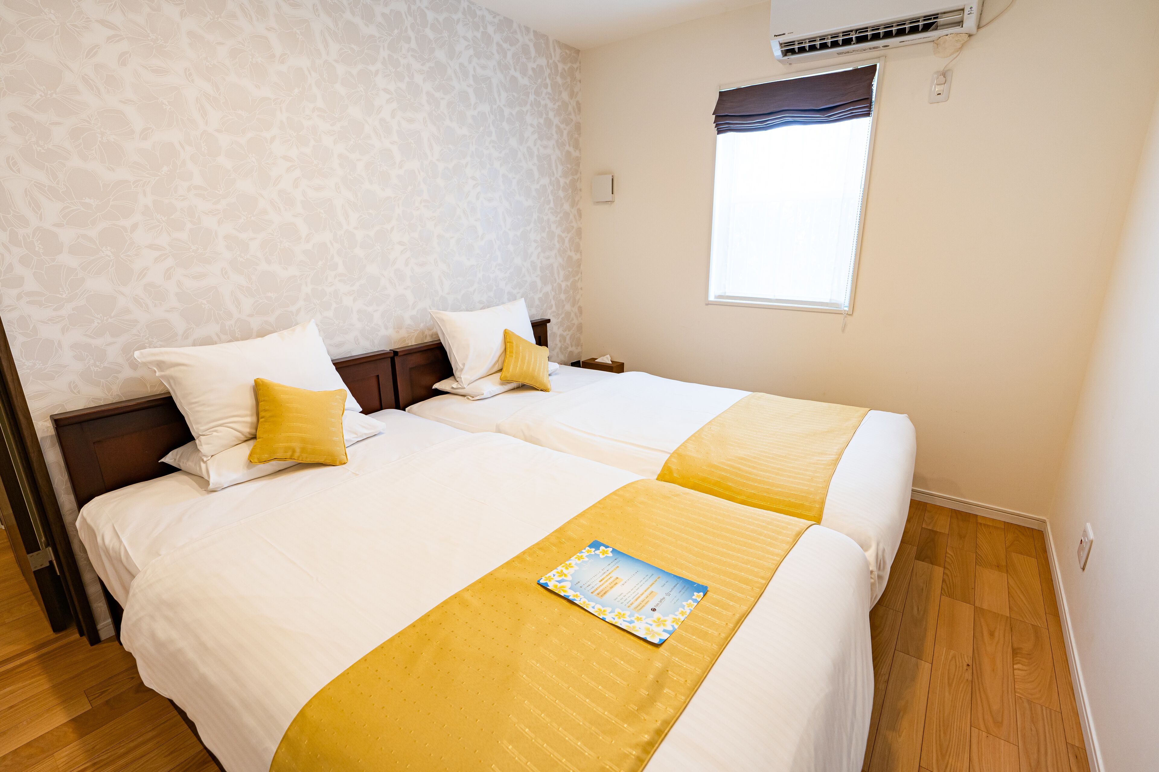 Habitación de hotel con dos camas, una ventana y aire acondicionado instalado en la pared.