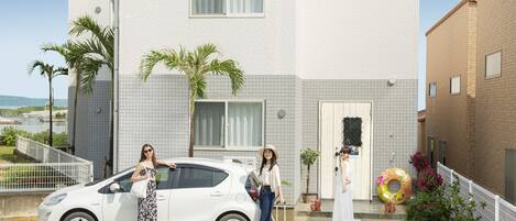 Un coche blanco estacionado en un estacionamiento, con un edificio al fondo.